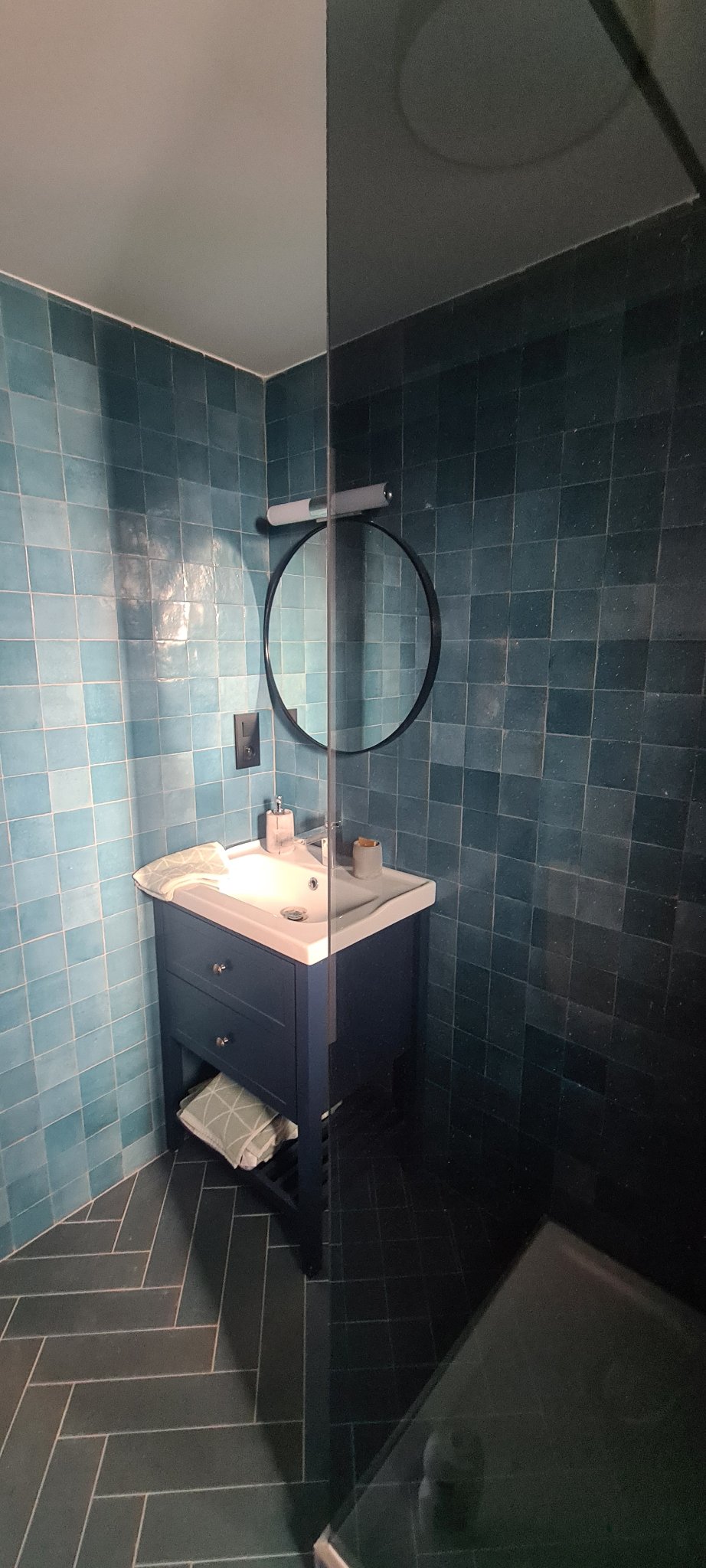 Ein Badezimmer mit blauen Fliesen, rundem Spiegel und blauem Waschtisch