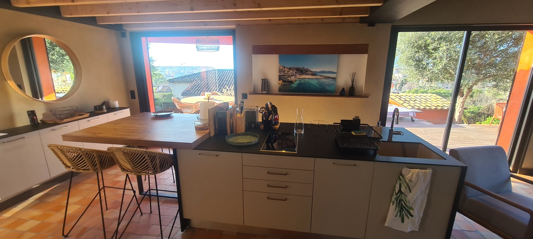 The open kitchen and living room with a wooden island and bar stools, sliding doors open to the terrace