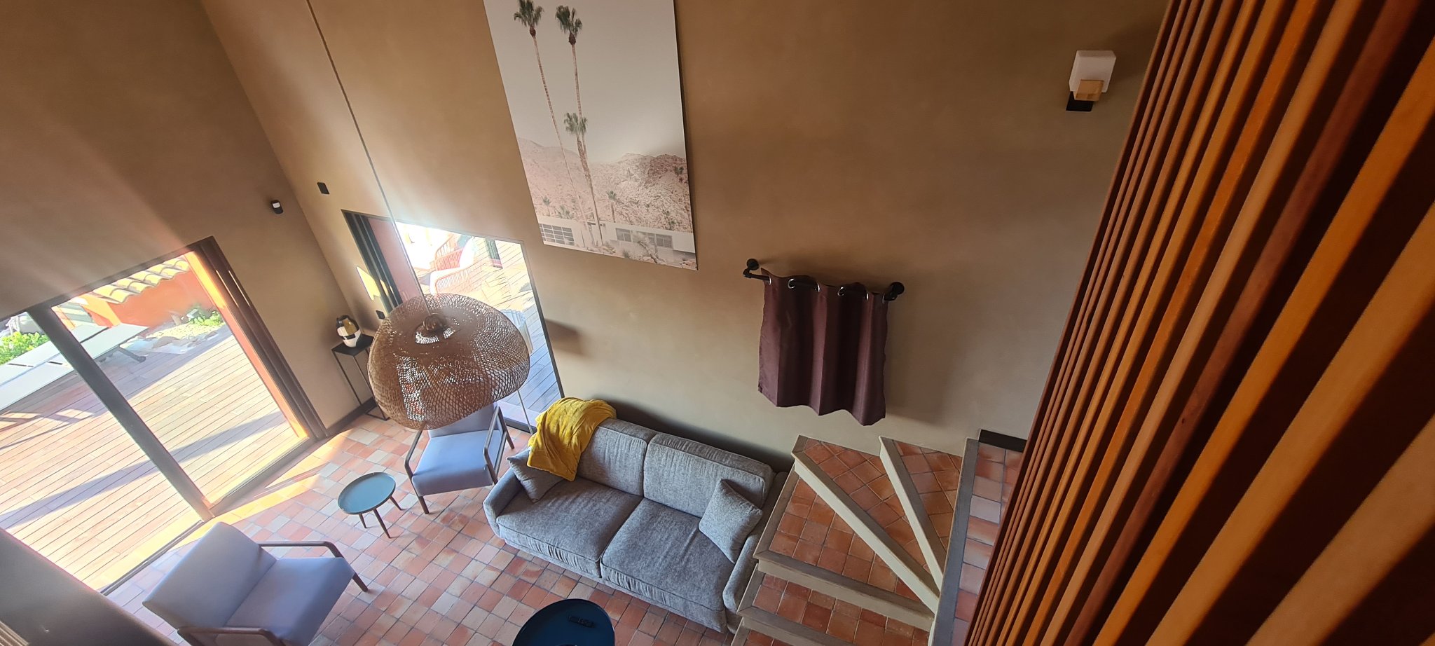 The living room seen from the mezzanine with the sofa and a door open to the terrace, sample evening scene